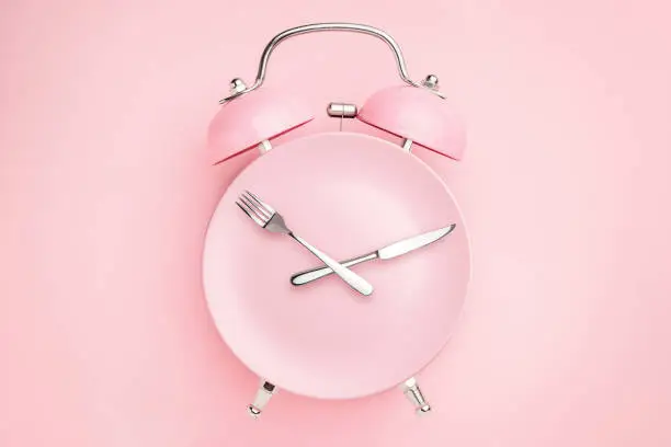 Photo of Alarm clock and plate with cutlery . Concept of intermittent fasting, lunchtime, diet and weight loss