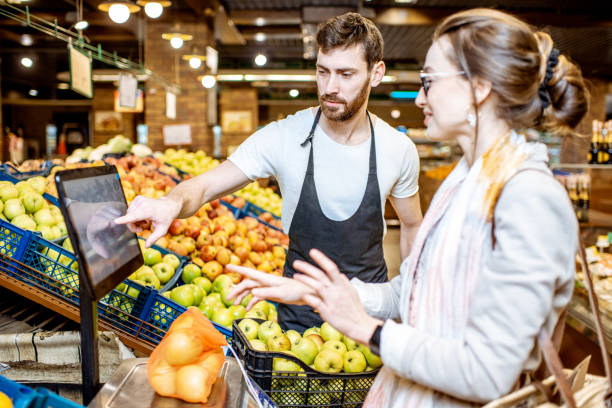 trabajadora ayudando a la mujer a pesar las frutas en el supermercado - weight scale apple comparison balance fotografías e imágenes de stock