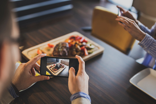 Couple sitting at a restaurant table, taking photos of food they have ordered before lunch