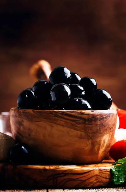 Photo of Spanish black olives in olive wooden bowl, rustic kitchen table, selective focus