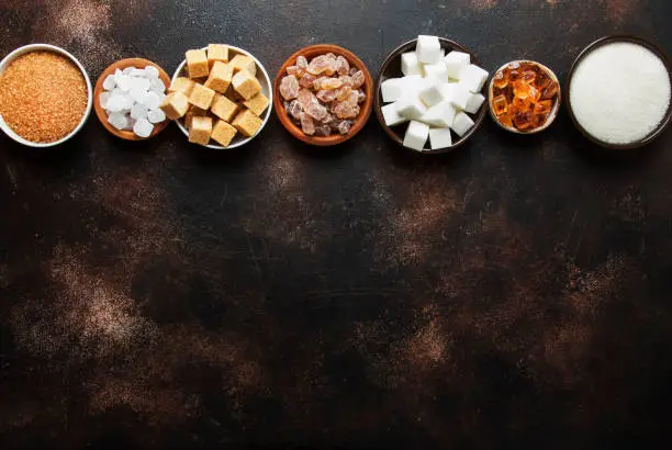 Photo of Set of different white and brown sugar in assortment, dark background, top view