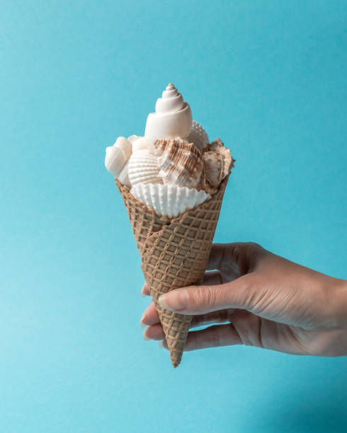 Creative composition with seashells and ice cream cone on pastel blue background. Summer minimal concept.