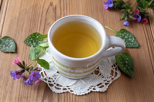 A cup of herbal tea with fresh lungwort, or pulmonaria flowers on a table