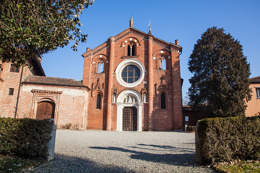 Church of Viboldone, with bell tower, arches, statues and trees during a sunny day in the countryside of Milan.