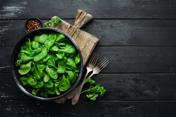 istock Fresh spinach. In a black plate on a wooden background Top view. Free space for your text. Flat lay 1139337745