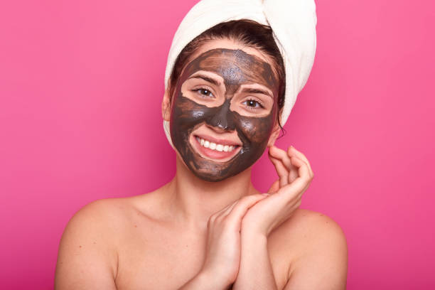 skin care concept. pleased young woman with toothy smile, has cocholate facial mask, isolated on pink background, has natural beauty, wears white towel and has nacked shoulders, keeps hands near face. - chocolate spa treatment alternative therapy towel imagens e fotografias de stock