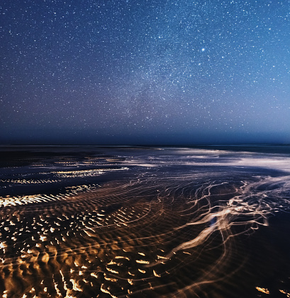 Bubbles of foam flow across smooth sand under Spring night skies.  Long exposure.