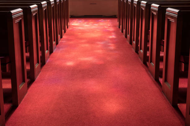 istock Light rays from stained glass window light up church aisle 1139344183