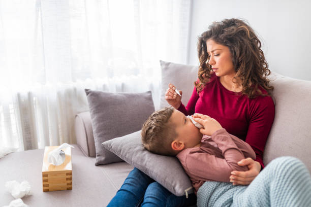 istock Sick boy with thermometer laying in bed and mother hand taking temperature 1139349611