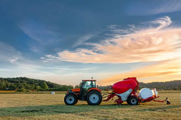Tractor with silage bale machine in rural landscape