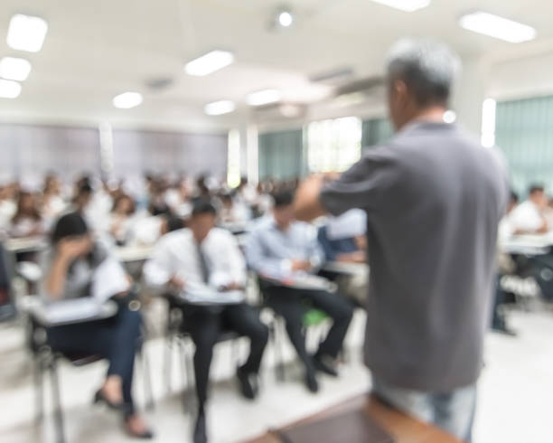 istock Blur background university students sitting in seminar lecture room with rear view teacher in front of class room 1139369740