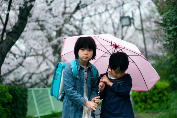 A elder sister and little brother is carrying an umbrella together in the dusk.