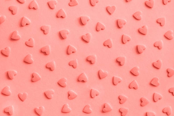 Love romantic pattern. Pink confectionery hearts sprinkles on pink, background, texture Coral toned stock photo