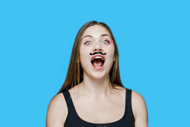 Young caucasian woman with drawn moustache on her face, screaming opening the mouth. Funny, humor concept. Young caucasian woman with drawn moustache on her face, screaming opening the mouth. Funny, humor concept. Studio, model, blue background, copy space. women movember mustache facial hair stock pictures, royalty-free photos & images