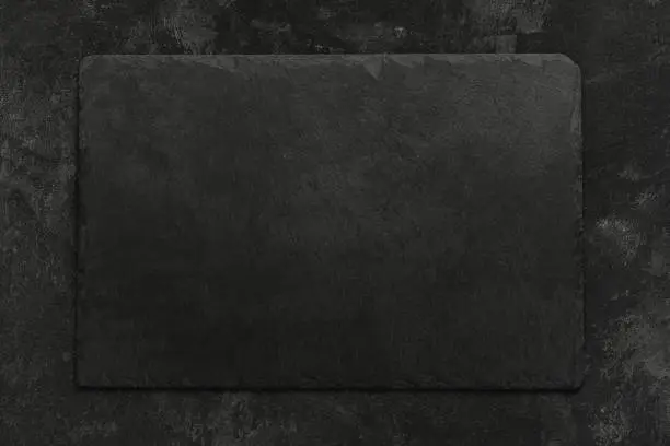 Photo of Black on black. Empty black granite stone rectangle board on black textured cement background, top view vith copy space for your text.