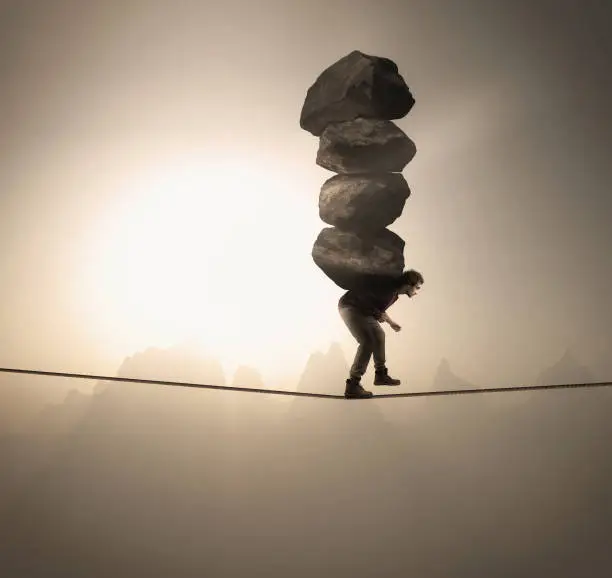 Photo of Man carries a stack of big rocks while balancing on a rope at high altitude .