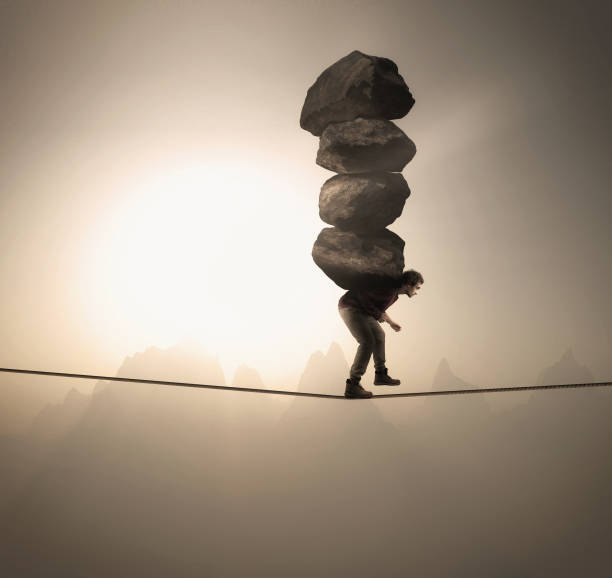man carries a stack of big rocks while balancing on a rope at high altitude . - business struggle imagens e fotografias de stock