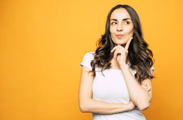 istock Let me think. Musing nice-looking girl next to the orange background in basic outfit is thinking about something and we can see it through her gestures and mimic. 1139415617