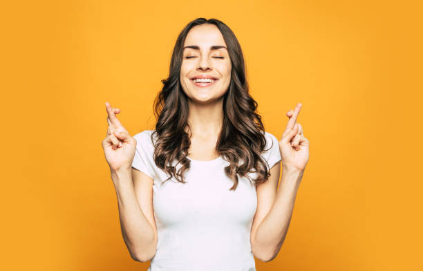 hacer creer. chica hermosa en un estado de ánimo de ensueño está cruzando los dedos como un símbolo de sus sueños para convertirse en un verdadero junto al color de soñar-naranja. - fingers crossed fotografías e imágenes de stock