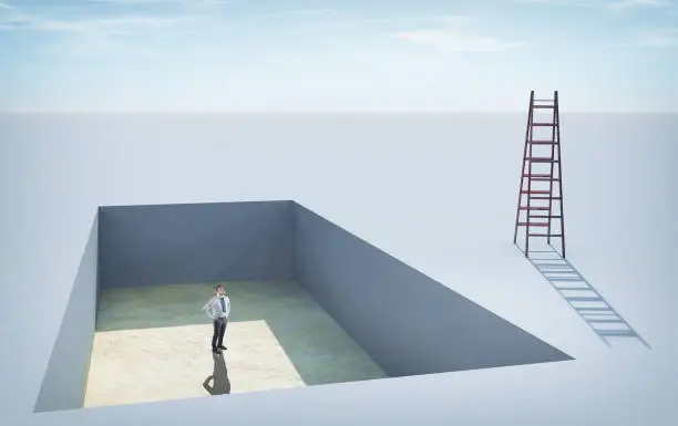Businessman standing in a  pit , looking up to a ladder.