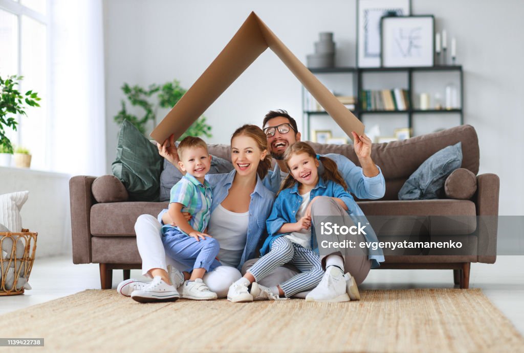 concept of housing and relocation. happy family mother father and kids with roof at home concept of housing and relocation. happy family mother father and kids with roof at a  home Family Stock Photo