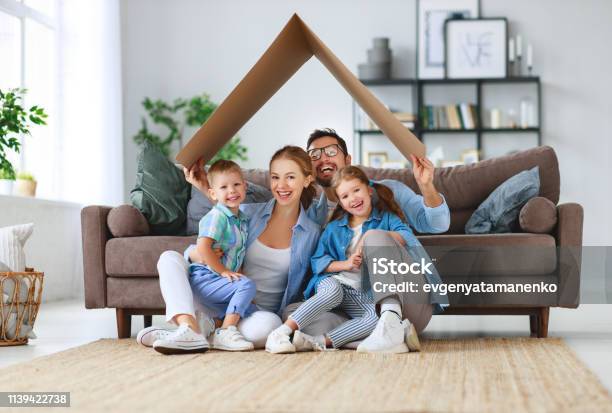 Concept Of Housing And Relocation Happy Family Mother Father And Kids With Roof At Home Stock Photo - Download Image Now