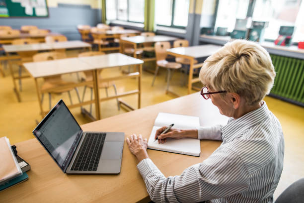 professeur aîné souriant prenant des notes dans la salle de classe. - grading photos et images de collection