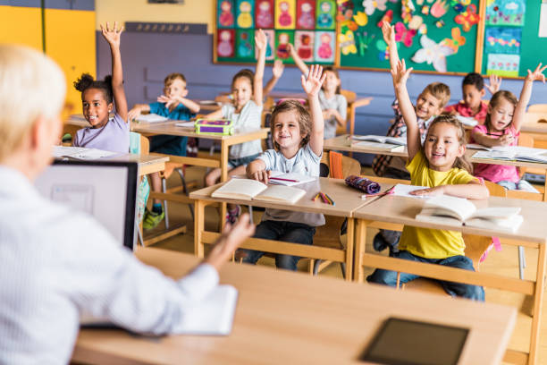 istock Large group of happy elementary students raising hands to answer the teacher's question on a class. 1139435287