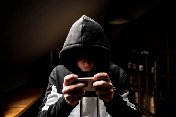 istock male hacker in the hood using a mobile phone, stealing your personal data f 1139450435
