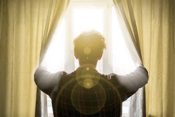 istock young male opens curtains window in the morning with light rays come in d 1139451880