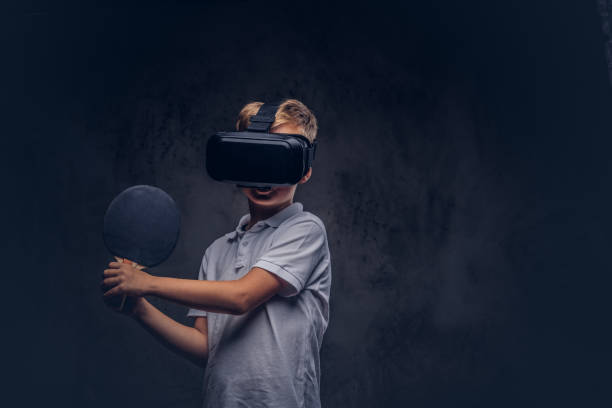 little redhead boy dressed in a white t-shirt playing ping-pong with a virtual reality glasses. isolated on dark textured background. - tennis teenager little boys playing imagens e fotografias de stock