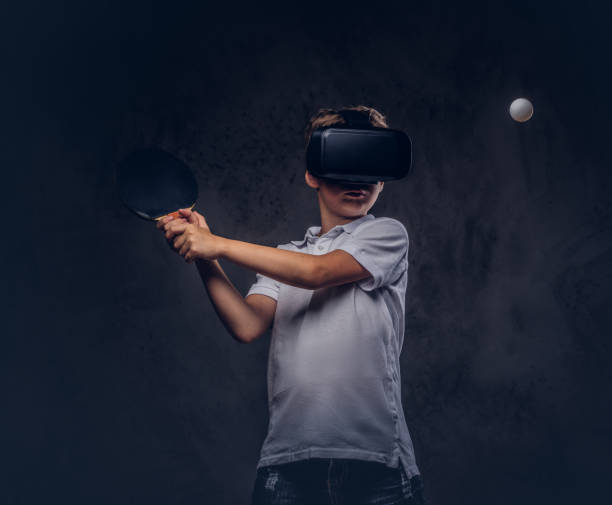 little redhead boy dressed in a white t-shirt playing ping-pong with a virtual reality glasses. isolated on dark textured background. - tennis teenager little boys playing imagens e fotografias de stock