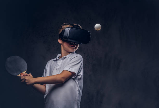 little redhead boy dressed in a white t-shirt playing ping-pong with a virtual reality glasses. isolated on dark textured background. - tennis teenager little boys playing imagens e fotografias de stock