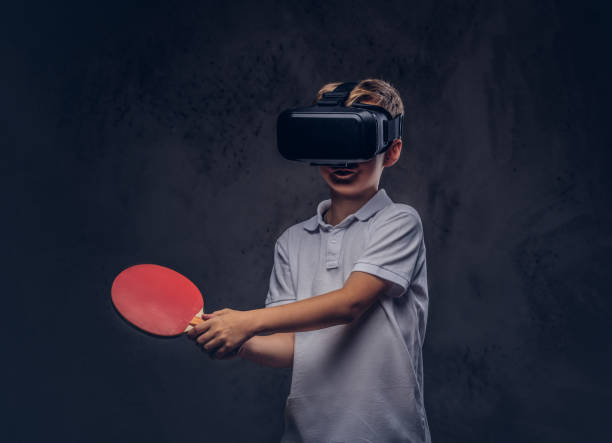 little redhead boy dressed in a white t-shirt playing ping-pong with a virtual reality glasses. isolated on dark textured background. - tennis teenager little boys playing imagens e fotografias de stock