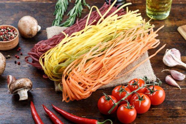 istock uncooked multi-colored spaghetti on a wooden table with vegetables. 1139458082