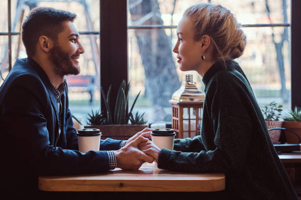 Attractive young couple holding hands, looking at each other and talking while sitting in the restaurant. stock photo