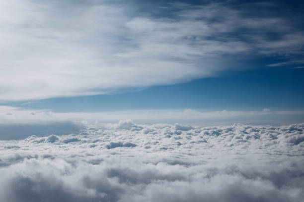 Airplane window view over horizon covered by white clouds beneath sunny blue sky.