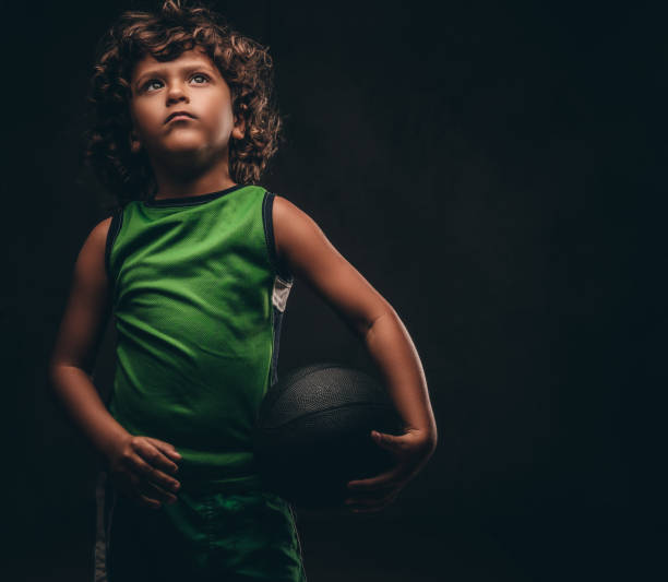 mały koszykarz w odzieży sportowej trzymającej piłkę w studio. izolowane na ciemnym tle teksturowanym. - child basketball uniform sports uniform zdjęcia i obrazy z banku zdjęć
