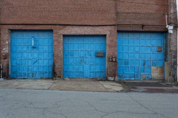 istock Three large blue garage doors on the back of an abandoned crumbling red brick warehouse 1139466688