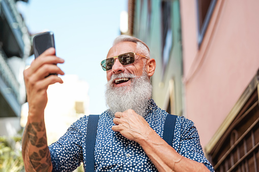 Bearded senior using mobile phone outdoor - Hipster mature man having fun with new trends smartphone apps - People lifestyle, technology and social influencer concept