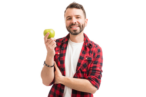 Good looking man in plaid shirt holding an apple and smiling on white