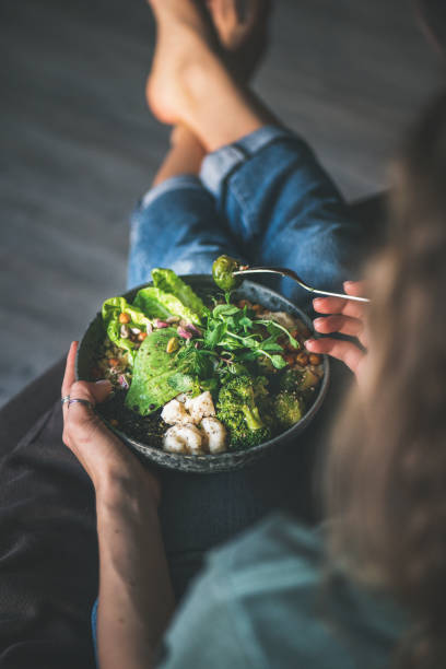 mujer sentada en casa y comiendo superbowl vegano - vegetal con hoja fotografías e imágenes de stock