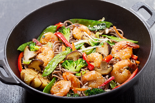 Stir fried noodles with shrimps and vegetables in a wok on dark background