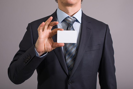 Closeup card in right hand of blue shirt businessman on gray background.