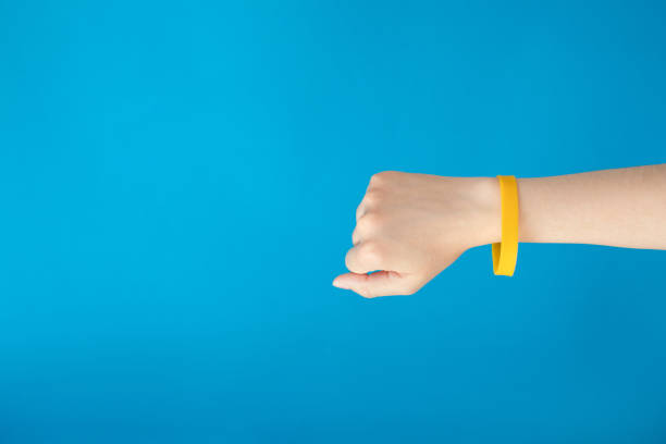 Female hand with empty yellow bracelet on blue background.  Clear sweat band mock up design. Music festival branding empty wristband design. bracelet photos stock pictures, royalty-free photos & images
