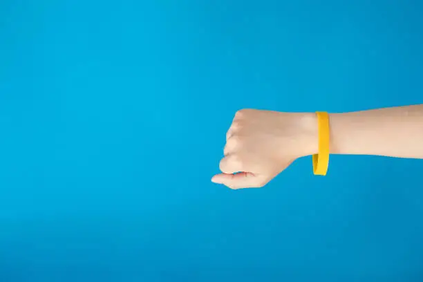 Photo of Female hand with empty yellow bracelet on blue background.  Clear sweat band mock up design.