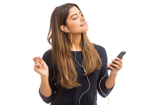 Young woman in casual using mobile phone and earphones against white background