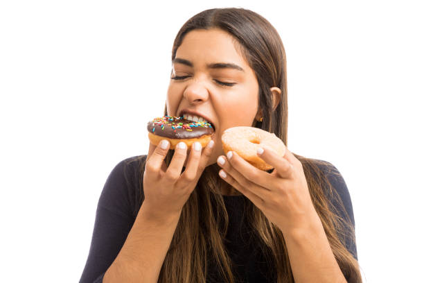 This Is One Of My Favorite Dessert Beautiful young woman with eyes closed biting piece of chocolate donut on white background greed photos stock pictures, royalty-free photos & images