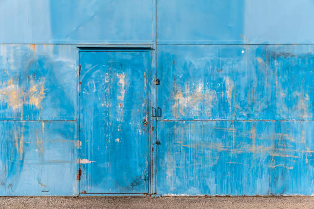 Background of a brick wall with a door in it. A round arch is above the door, made of stones. The wooden door is closed and smeared with blue paint.