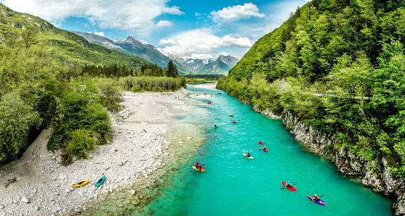 Group of people kayaking on the river Soča in Slovenia Europe. Scenic nature, with turquoise water river, surrounded with bushy forest in the summer time.